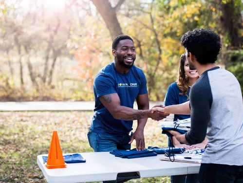 Gentleman standing behind a table, reaching out to shake a person's hand.