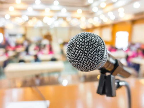 A simple image of a microphone at the front of a busy conference room.