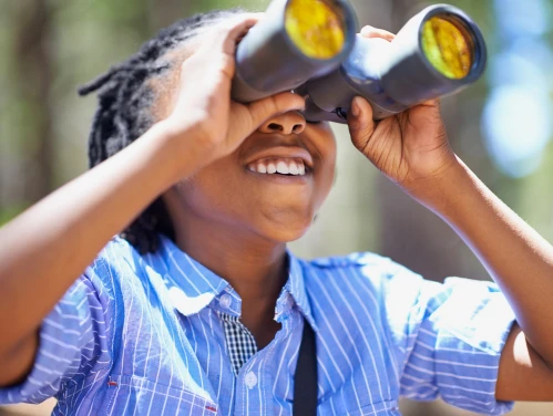Young boy with binoculars looking upward.