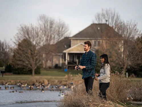 Man and woman fishing a small pond in a neighborhood setting.
