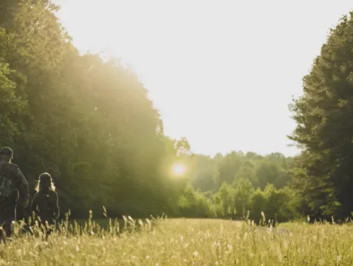 An adult mentor walking away from the camera with a young hunter in a field.