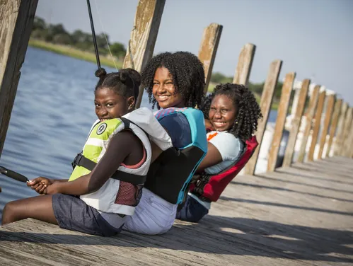 Three girls in lifejackets fishing off a dock