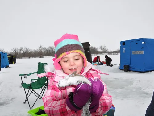 A young girl holding a trout she caught through the ice at a community trout stocking event