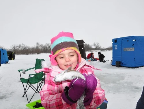 A young girl holding a trout she caught through the ice at a community trout stocking event