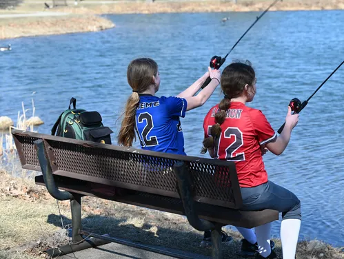 2 youth softball players in uniform fishing from a park bench