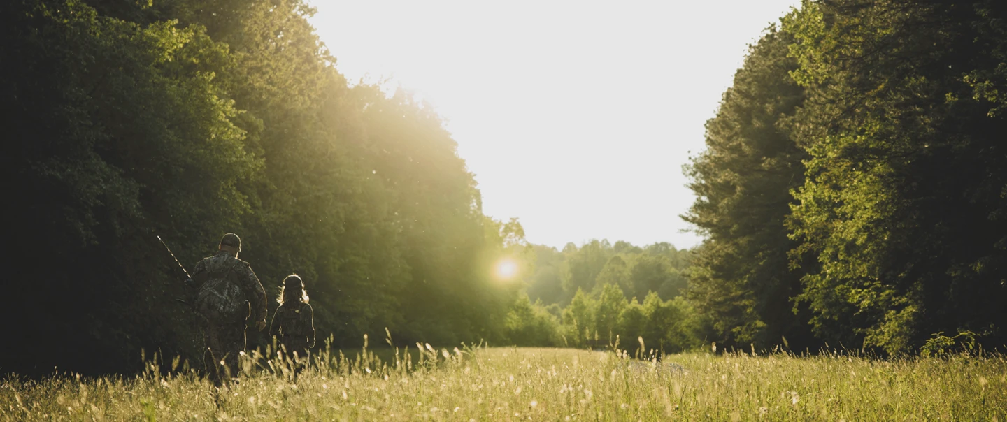 An adult mentor walking away from the camera with a young hunter in a field.