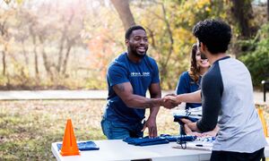 Gentleman standing behind a table, reaching out to shake a person's hand.