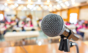 A simple image of a microphone at the front of a busy conference room.