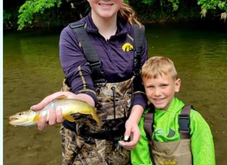 Girl and boy in stream with hipwaders, holding a trout.
