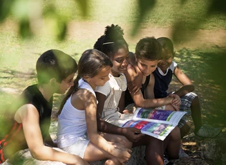 Group of kids outdoors, huddled around what look like educational worksheets.