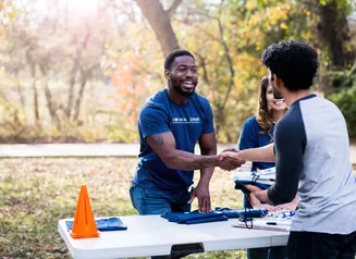 Gentleman standing behind a table, reaching out to shake a person's hand.