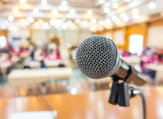 A simple image of a microphone at the front of a busy conference room.