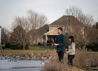 Man and woman fishing a small pond in a neighborhood setting.