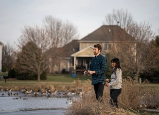 Man and woman fishing a small pond in a neighborhood setting.