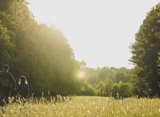 An adult mentor walking away from the camera with a young hunter in a field.