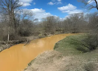 This image shows brown, murky water flowing at the South Branch of Lizard Creek in Fort Dodge