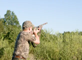 Young man shooting a shotgun into a blue sky, dove hunting.