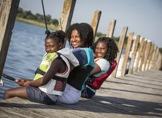 Three girls in lifejackets fishing off a dock