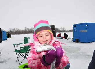 A young girl holding a trout she caught through the ice at a community trout stocking event