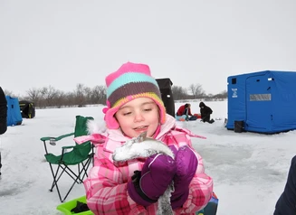 A young girl holding a trout she caught through the ice at a community trout stocking event