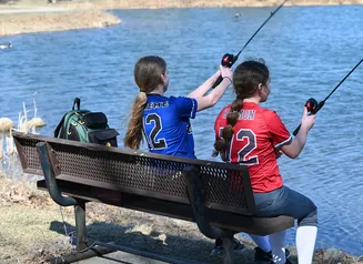 2 youth softball players in uniform fishing from a park bench